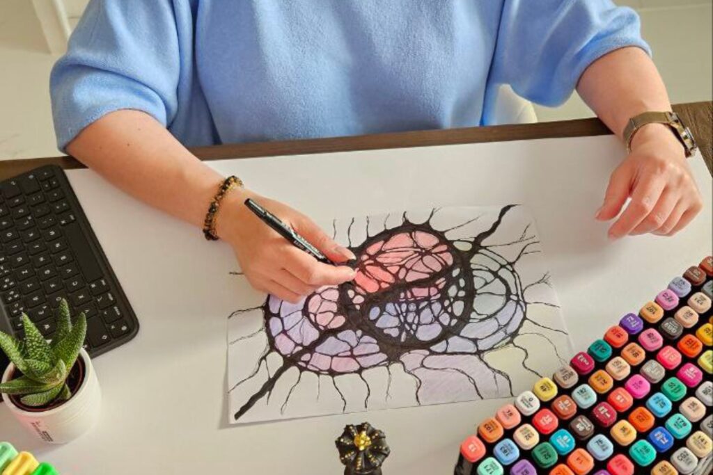 Pani Katarzyna tworzy neurografikę z pastelowymi i czarnymi liniami.